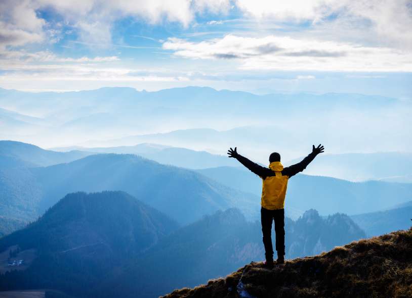 Man stands on mountain with arms raised above head